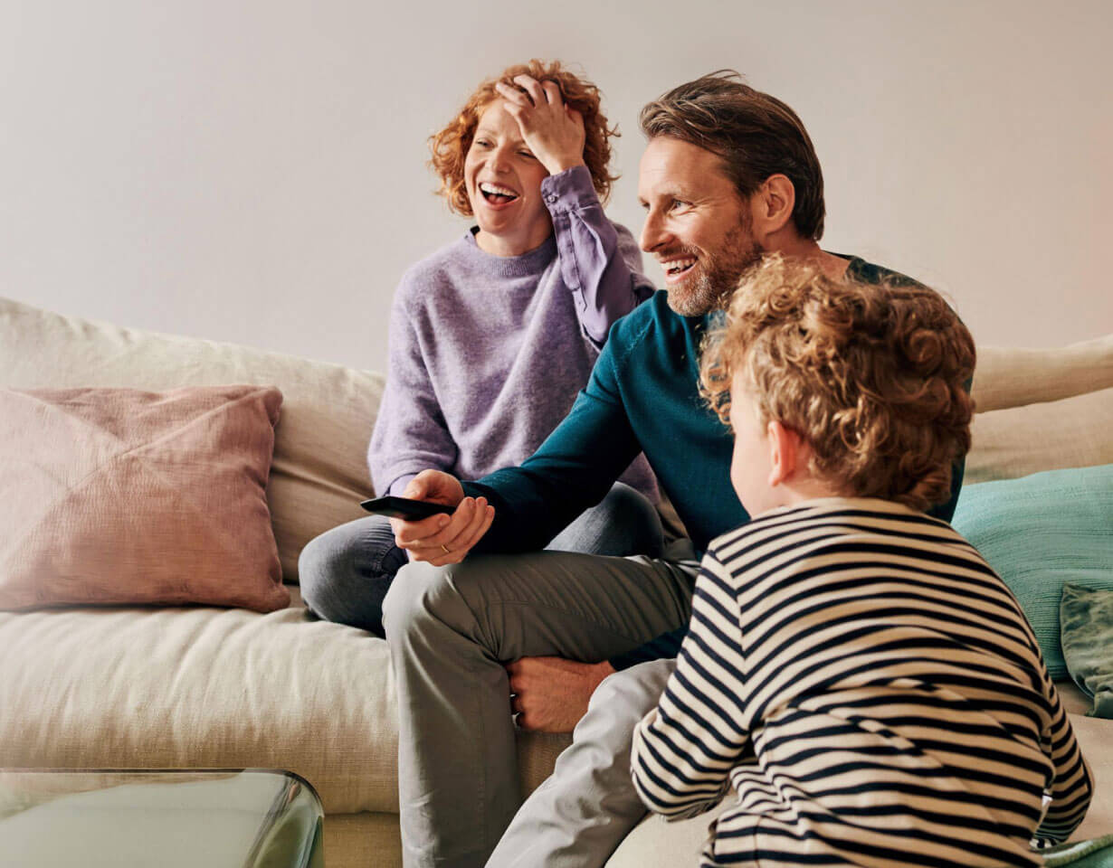 Lachende Familie beim Streaming im Wohnzimmer die sich das beste Telekom Internet gesichert hat