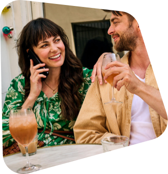 Eine lächelnde Frau im Gespräch auf einem Smartphone sitzt neben einem Mann mit Bart.