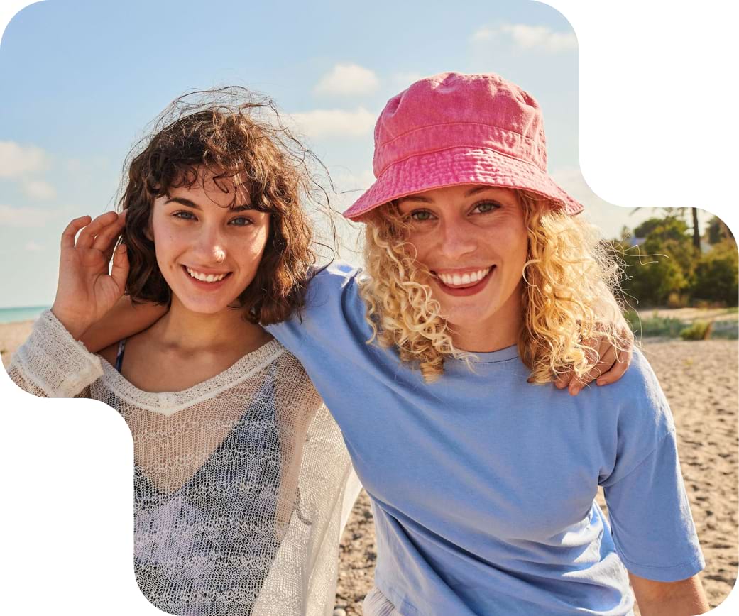 Zwei junge Frauen am Strand freuen sich über die Travel Mobil Optionen