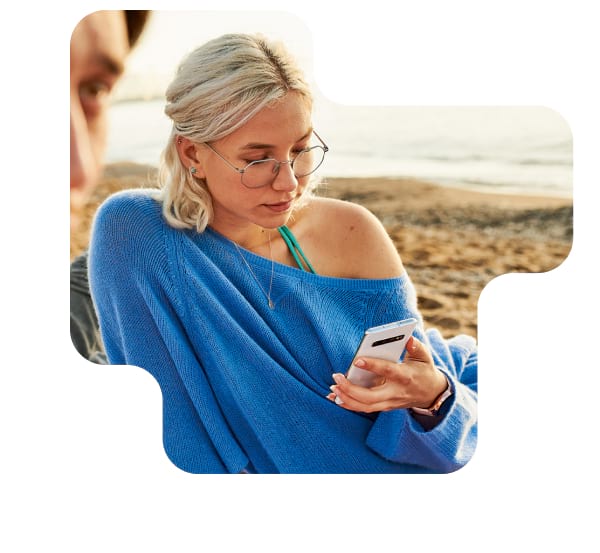 Junge Frau mit Smartphone informiert sich am Strand über Roaming-Gebühren