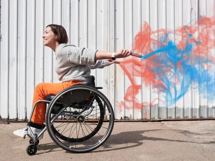 Person im Rollstuhl zaubert mit Rauchfackeln rote und blaue Farbwolken.