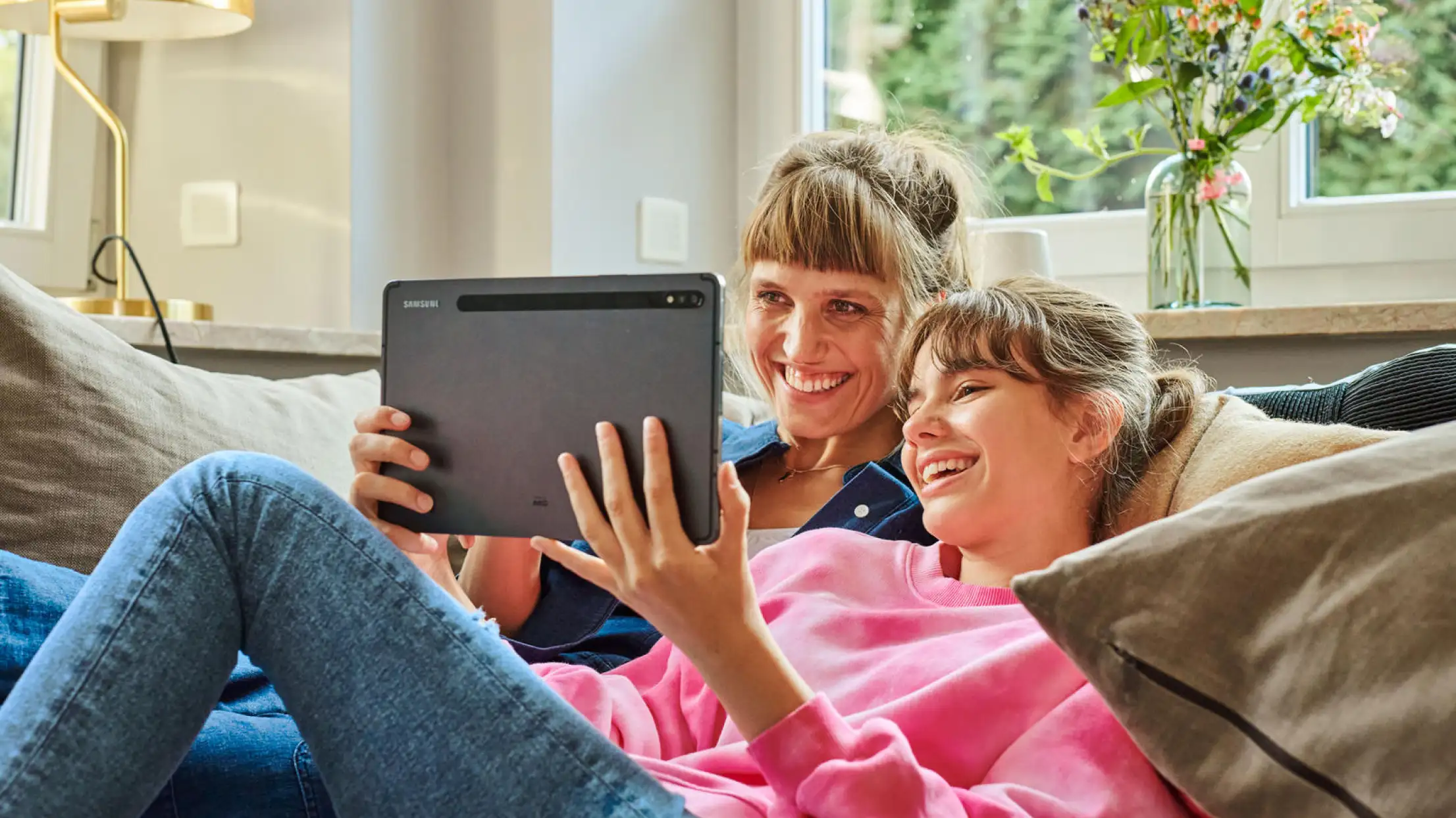 2 Personen sitzen auf dem Sofa und schauen zusammen auf ein Tablet
