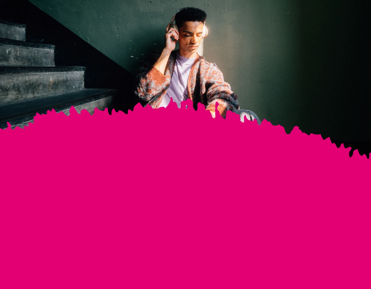 Ein junger Mann sitzt mit Kopfhörern auf den Treppen und genießt den MagentaMobil Young Vorteil