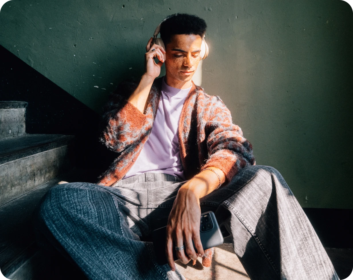 Ein junger Mann sitzt mit Kopfhörern auf den Treppen und genießt den MagentaMobil Young Vorteil