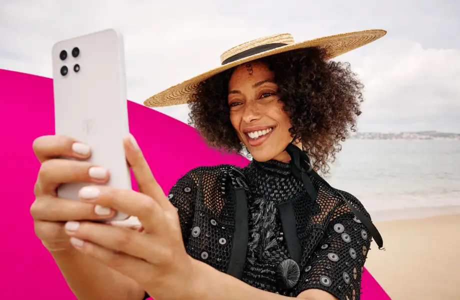 Person mit Strohhut am Strand macht ein Selfie mit weißem Smartphone.