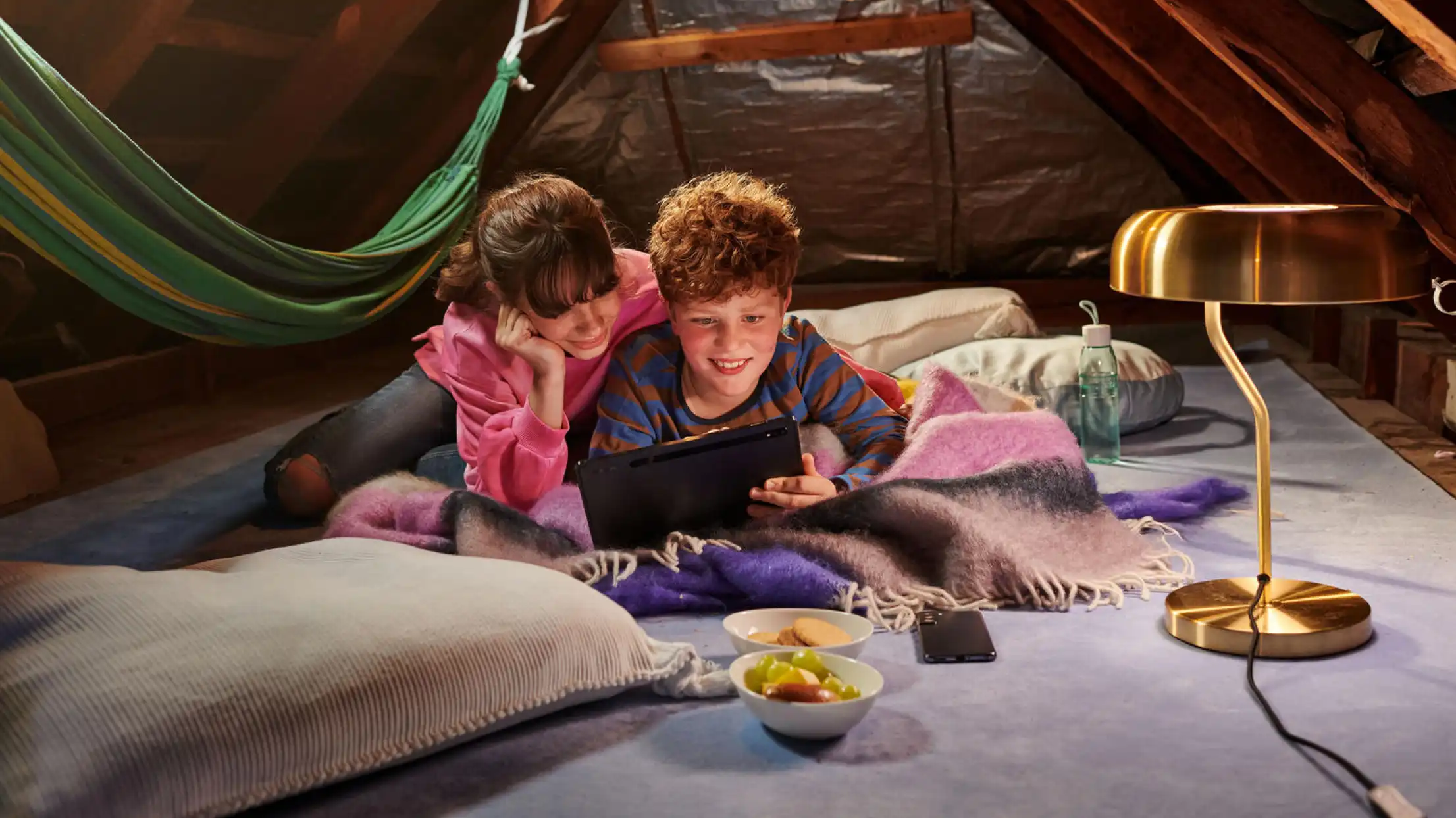 Zwei Jugendliche auf dem Dachboden schauen auf ein Tablet