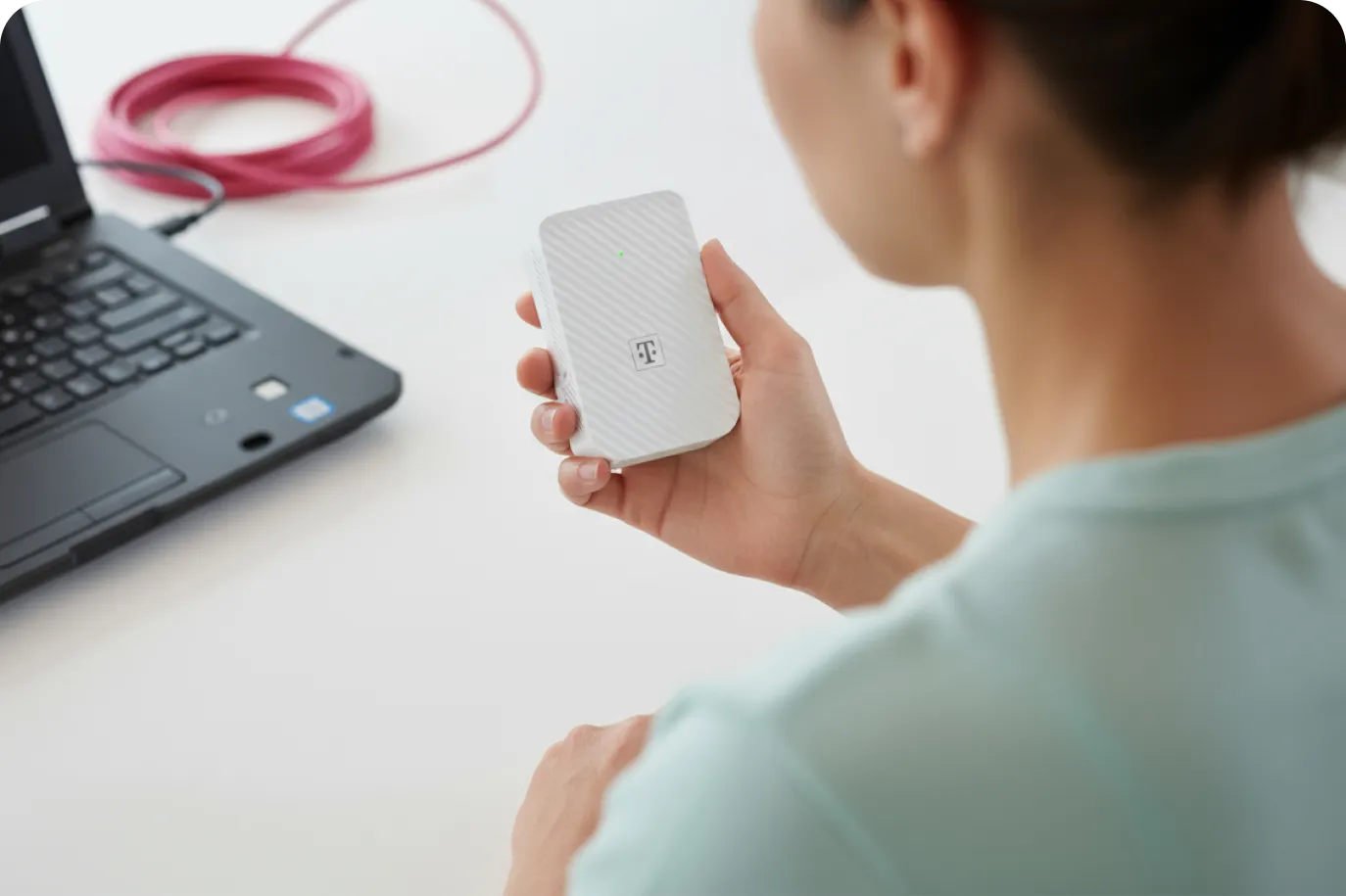 Eine Frau vor einem Laptop hält einen WLAN-Verstärker in der Hand