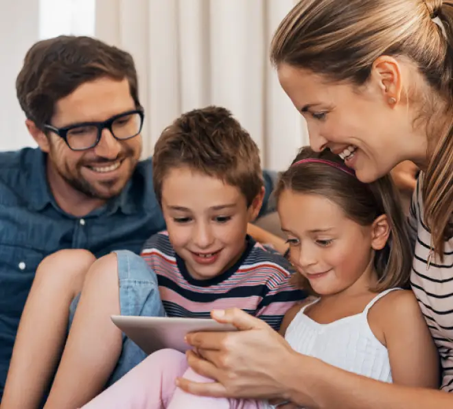 Eine Familie sitzt gemütlich auf dem Sofa und schaut gemeinsam auf ein Tablet.