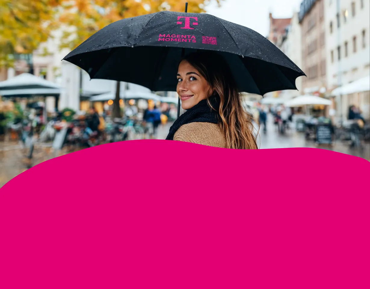 Person mit schwarzem Regenschirm mit T-Logo und Aufdruck Magenta Moments mit QR-Code in regennasser Innenstadt