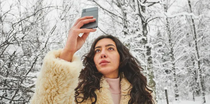 Eine Frau in einer Winterlandschaft schaut auf ihr Smartphone