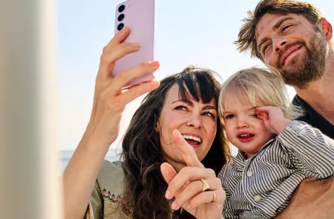 Familie am Strand, schaut gemeinsam auf ein Smartphone.
