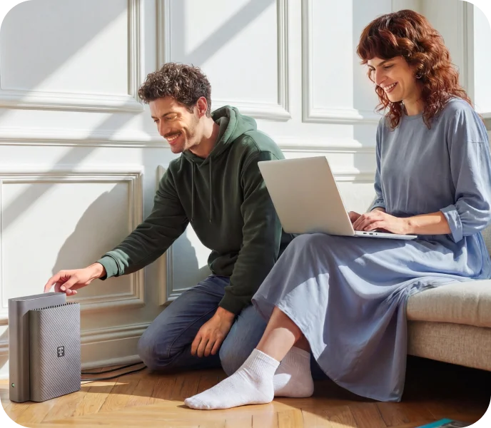 Mann richtet einen Telekom Router ein, während eine Frau daneben mit einem Laptop sitzt
