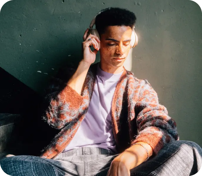 Junger Mann mit Kopfhörern sitzt auf einer Treppe.