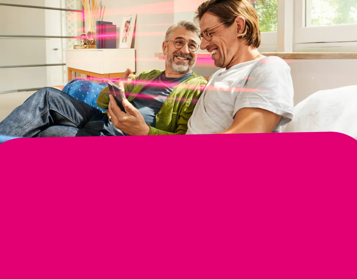 Zwei lächelnde Männer betrachten gemeinsam Inhalte auf einem Smartphone, während magenta Lichtstreifen eine schnelle Datenverbindung symbolisieren.
