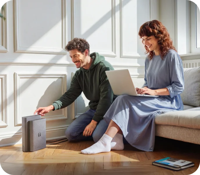 Mann richtet einen Telekom Router ein, während eine Frau daneben mit einem Laptop sitzt