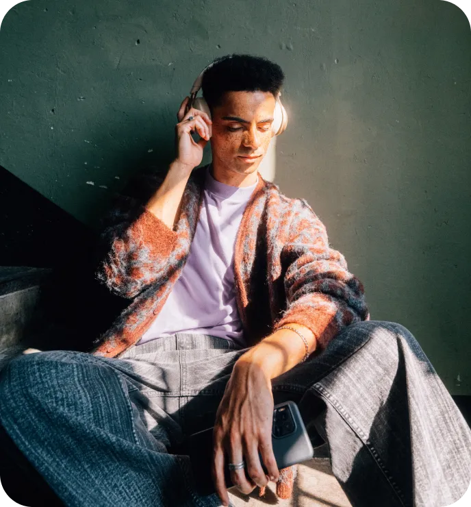 Junger Mann mit Kopfhörern sitzt auf einer Treppe.