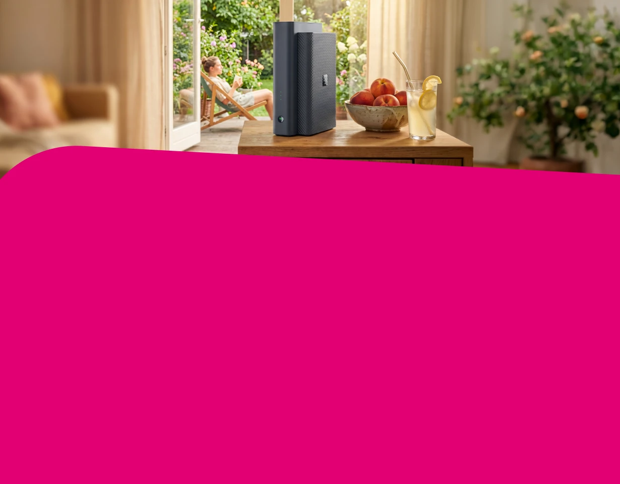 Ein Telekom Router steht auf einem Sideboard, im Hintergrund sitzt eine Frau entspannt im Gartenstuhl draußen. Neben dem Router stehen Pfirsiche und Limonade.