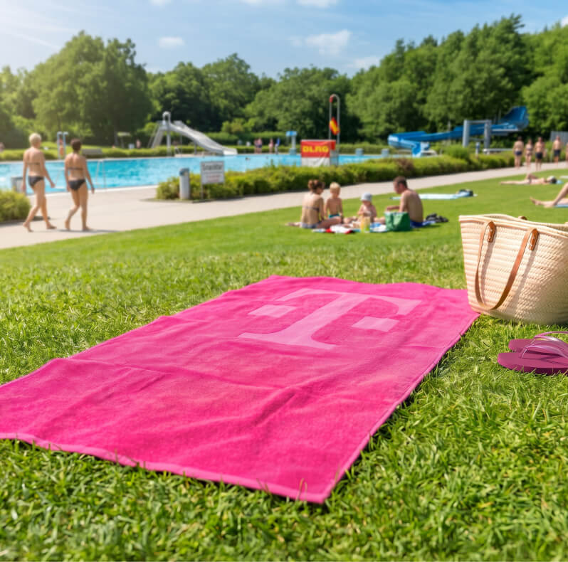 Handtuch mit Magenta-Logo auf der Wiese in einem Freibad