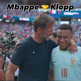 Kylian Mbappé und Jürgen Klopp umarmen sich lachend am Spielfeldrand. Text: Mbappe und Klopp