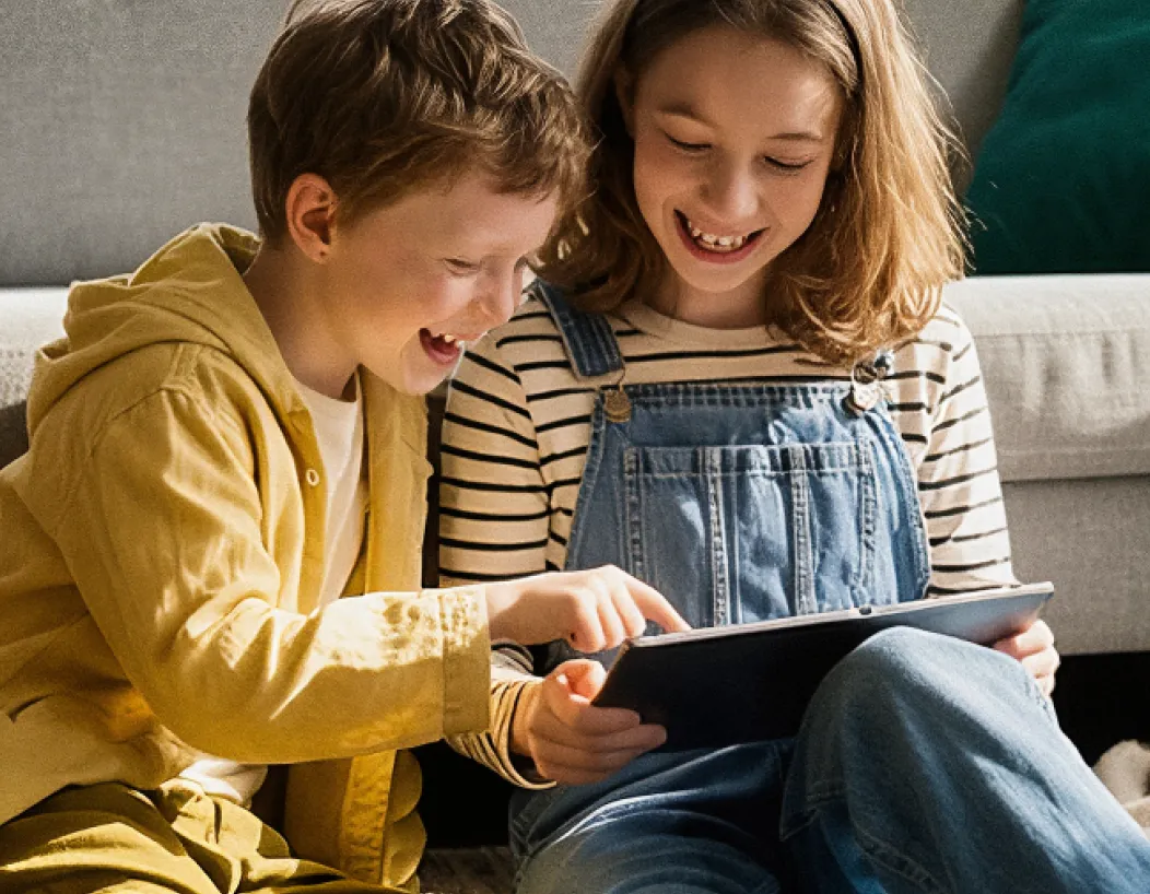 Zwei Kinder schauen lachend gemeinsam auf ein Tablet