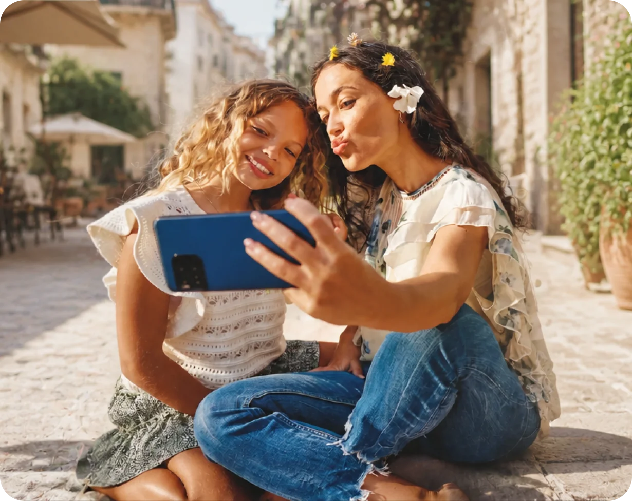 Zwei Frauen sitzen in einer sonnigen Gasse und machen gemeinsam ein Selfie mit dem Smartphone