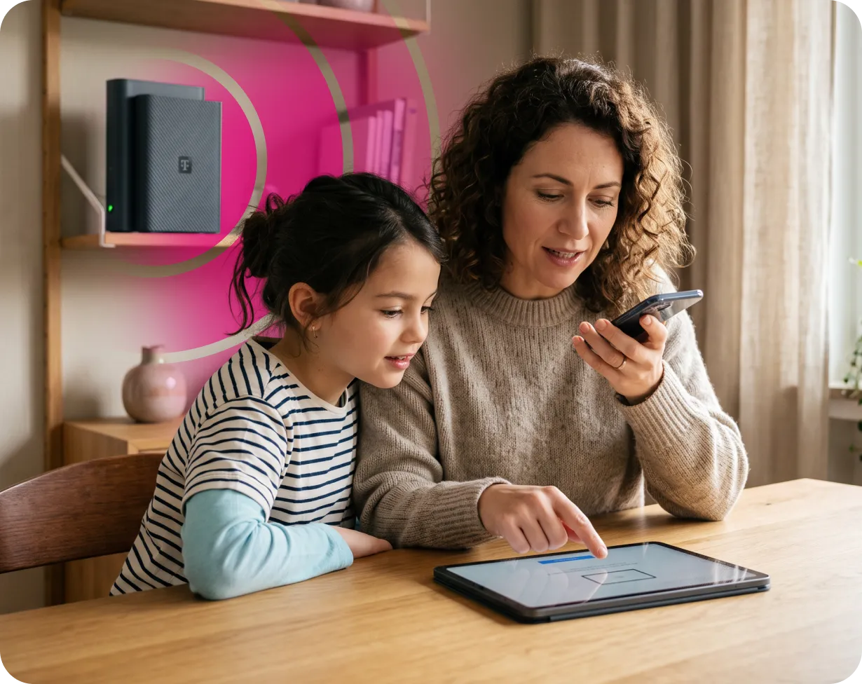 Mutter und Tochter am Tisch mit Tablet und Smartphone, im Regal ein Telekom Router